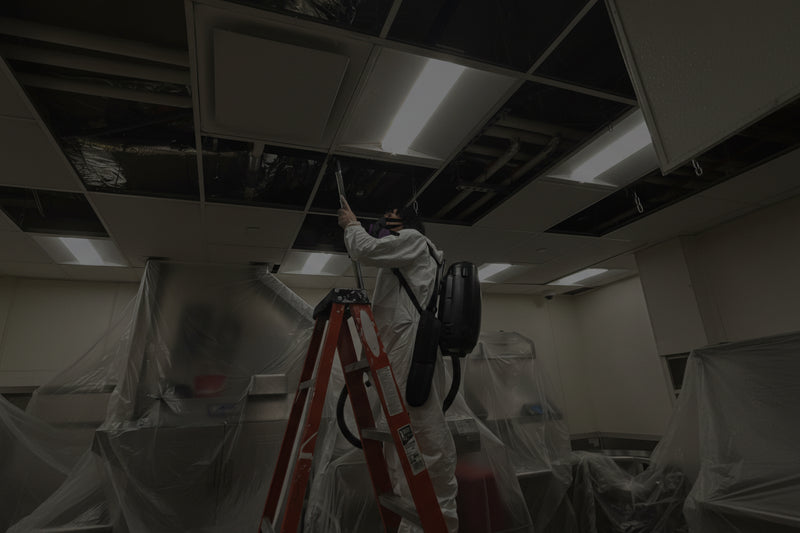 Person on a ladder repairing a ceiling with plastic sheeting covering the floor.