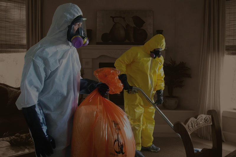 Two people in hazmat suits cleaning up a room with orange bags.