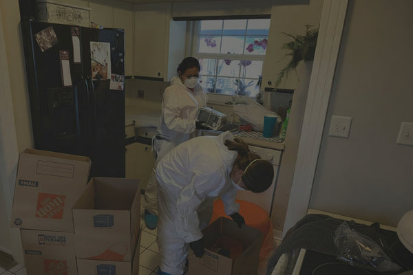 Two people in protective suits and masks in a kitchen with Home Depot boxes.