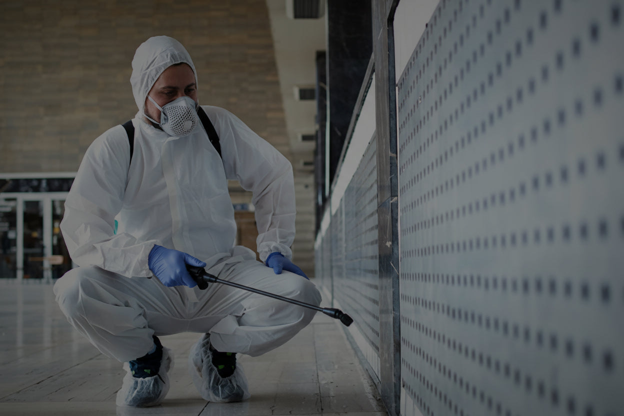 Person in full protective gear with a spray bottle in an indoor setting
