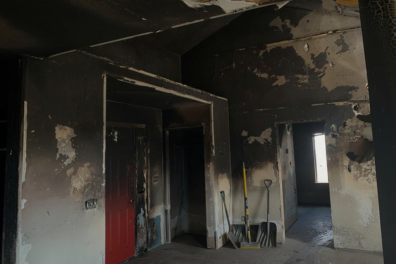 Burnt room with charred walls and a red door, showing signs of fire damage.